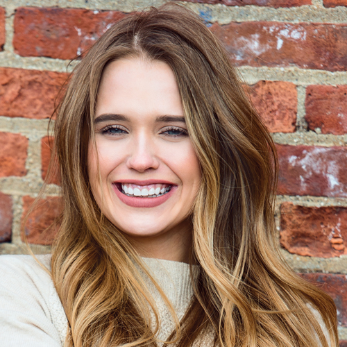 Beautiful happy girl drinking coffee and smiling near red brick wall